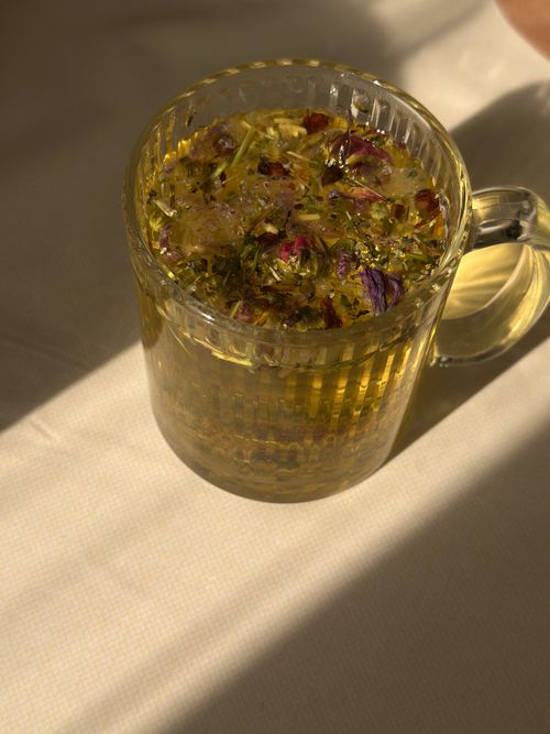 Free Glass mug containing herbal tea with dried flowers, bathed in warm sunlight on a table. Stock Photo