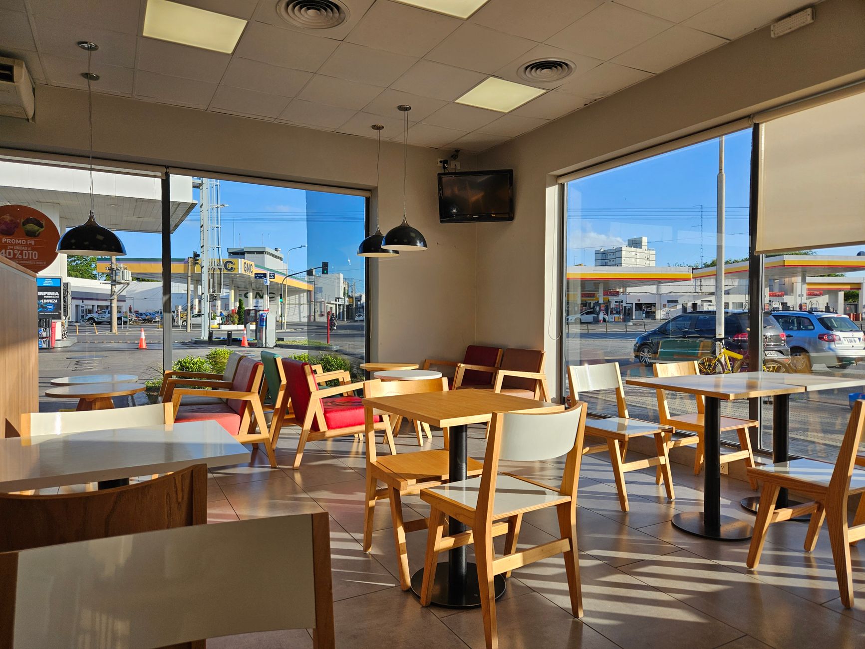 Empty modern cafe interior with large windows and wooden furniture on a sunny day.