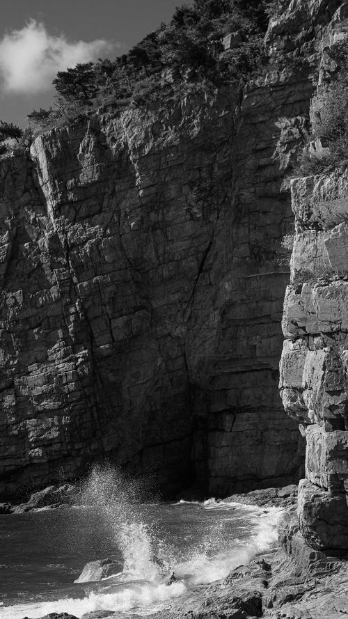 Free Black and white photo of imposing cliff with waves crashing below, evoking drama. Stock Photo