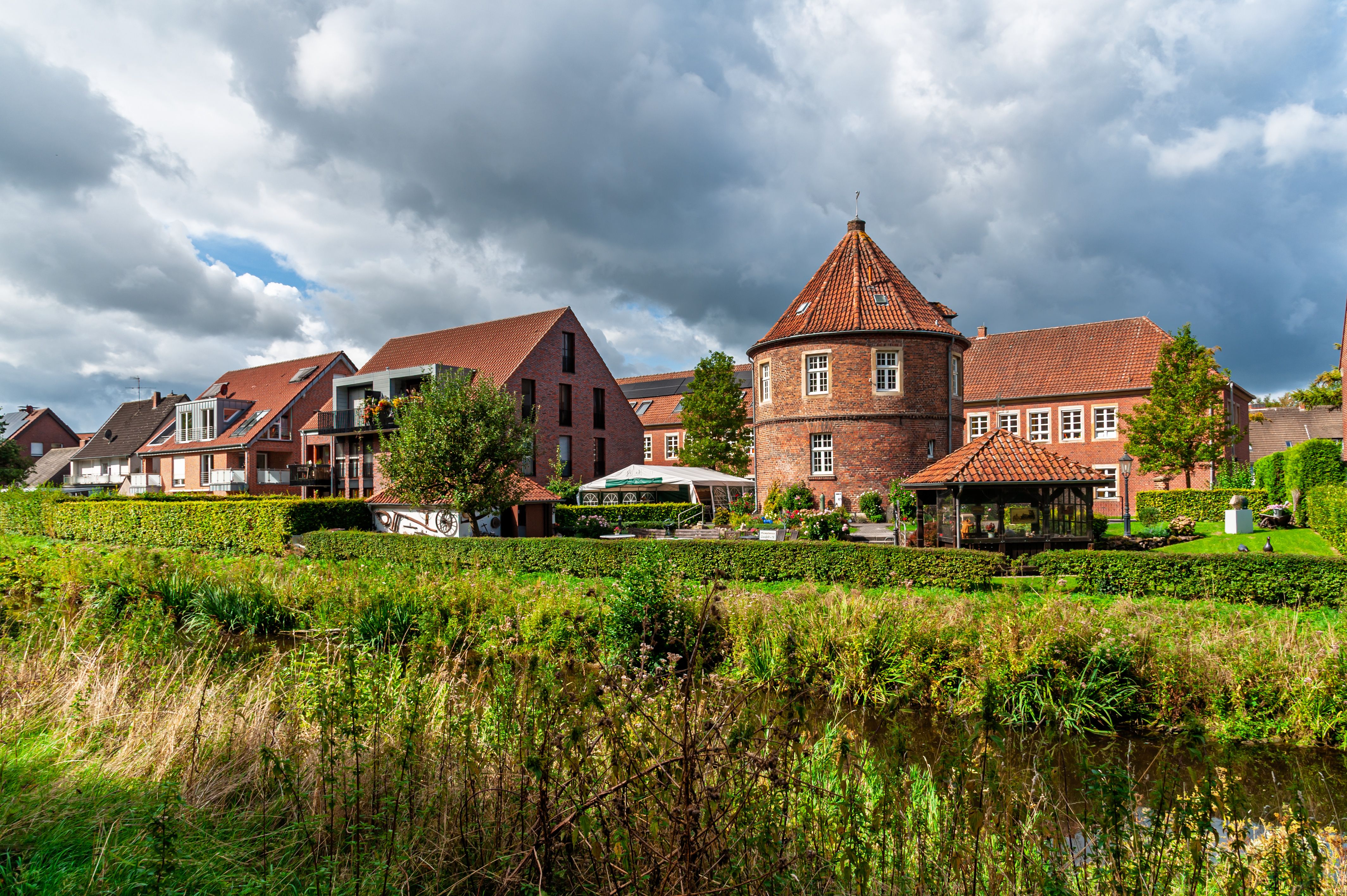 Quaint red brick buildings in Coesfeld, Germany with lush greenery under a dramatic sky.