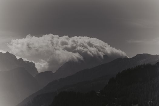 A dramatic mountain scene with dense clouds forming over rugged terrain, captured in monochrome.