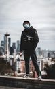 一名蒙面男子手持咖啡，站在屋顶上，背景是西雅图的天际线