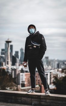 一名蒙面男子手持咖啡，站在屋顶上，背景是西雅图的天际线