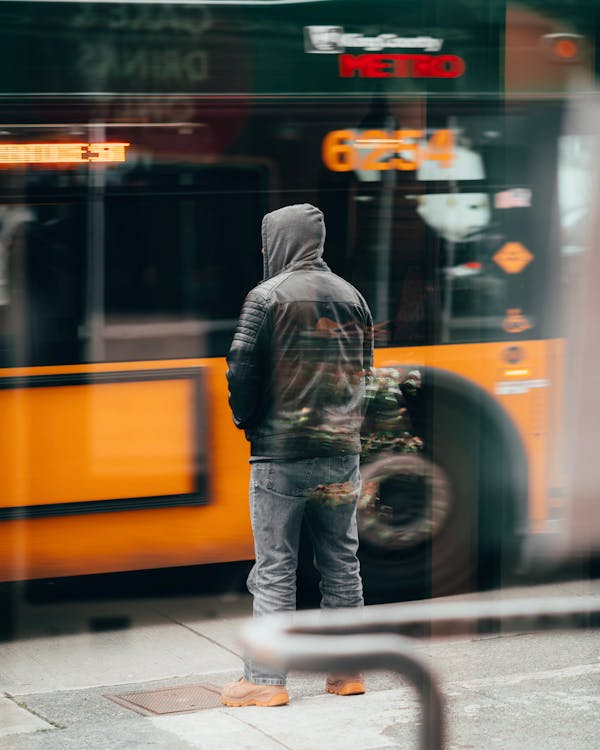 黄色いバスの前に立っている黒いジャケットと青いデニムジーンズの男