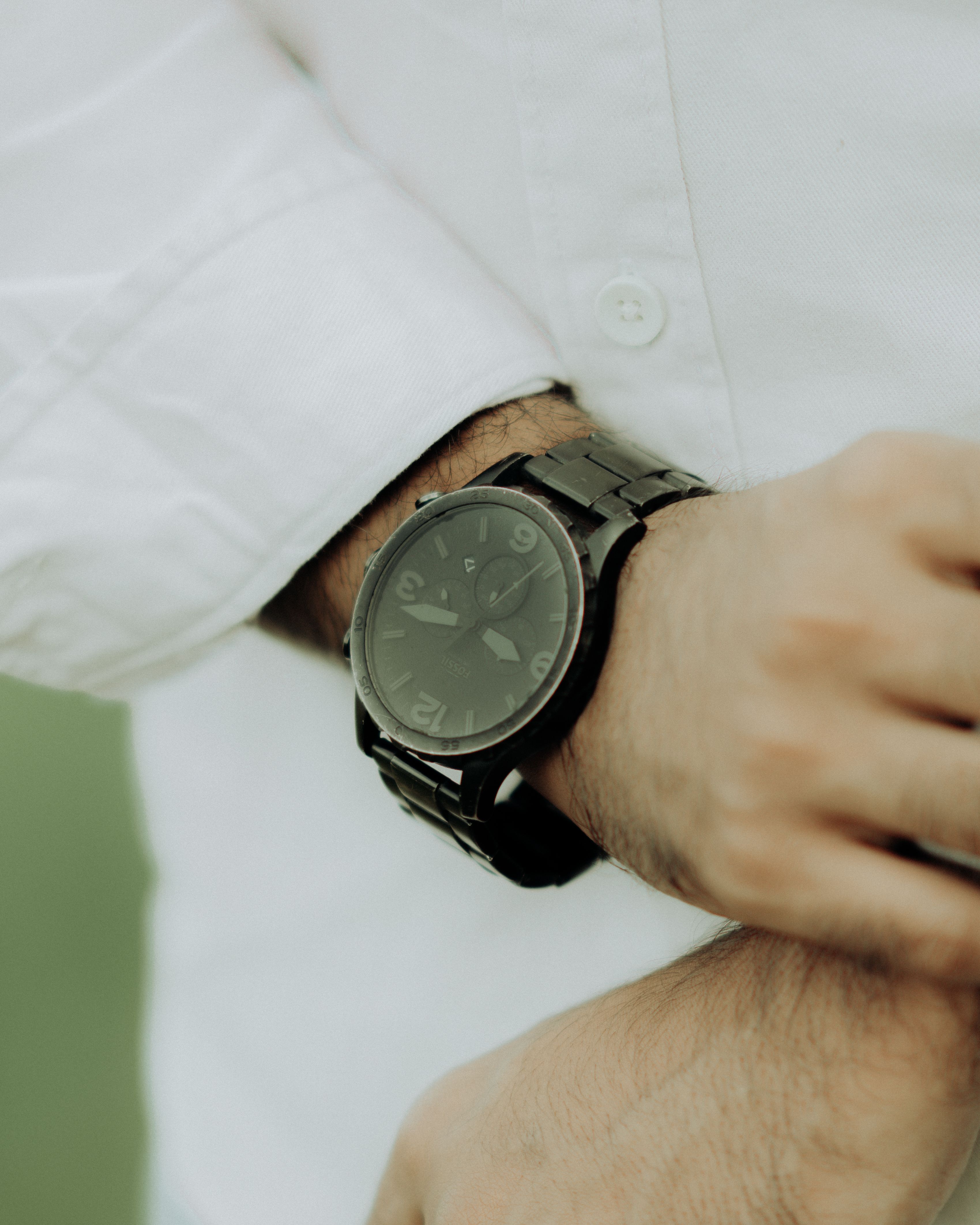 Close-up shot of a sleek black wristwatch on a person's wrist wearing a white shirt.