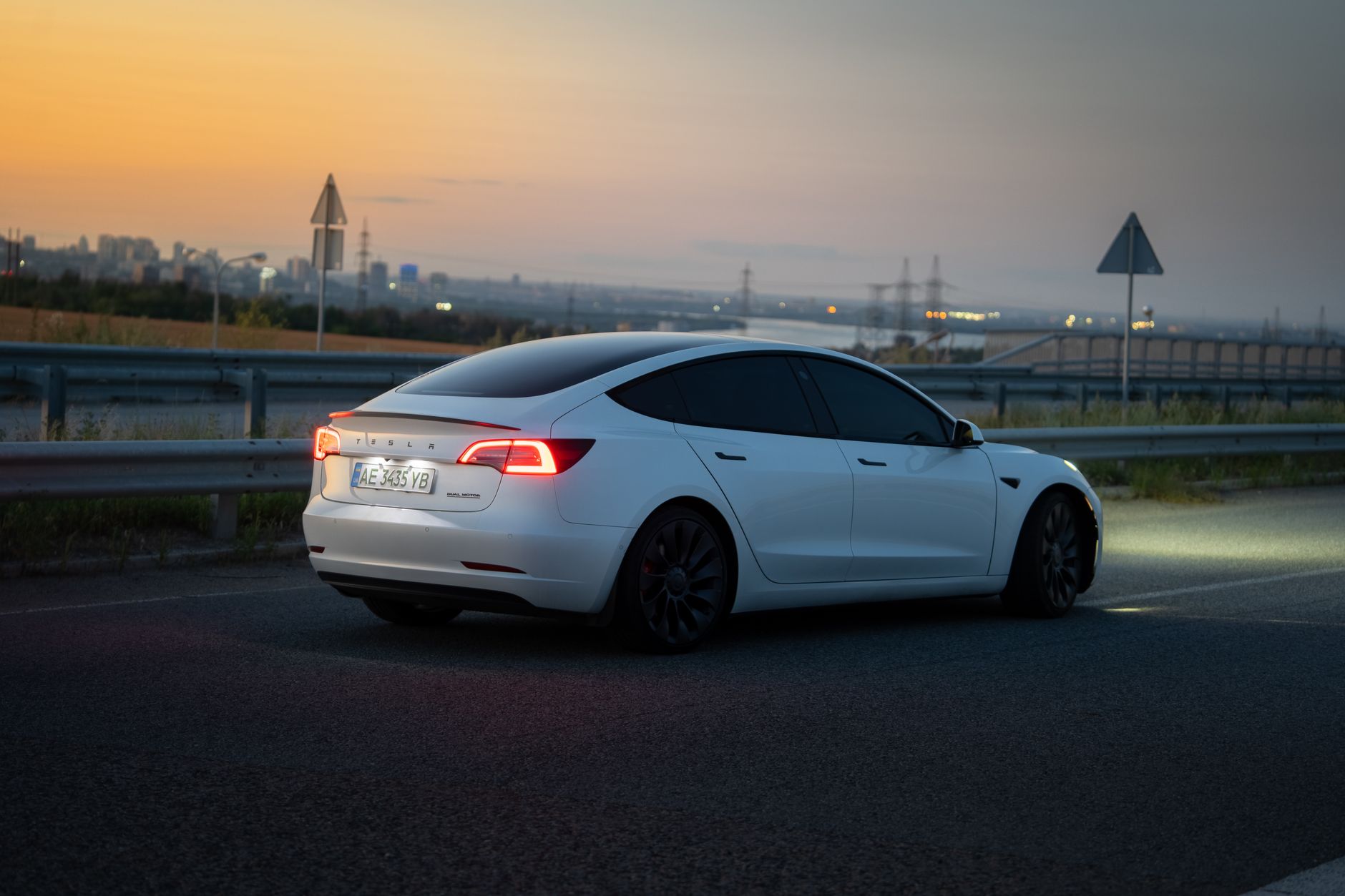 Electric car on the highway during twilight in Dnipro, Ukraine, showcasing urban backdrop.