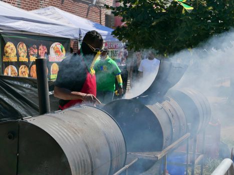 Man cooking on a drum grill at a lively street festival in New York City.