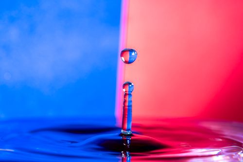 Free Dynamic macro shot of a water droplet splash against a vivid blue and red background. Stock Photo