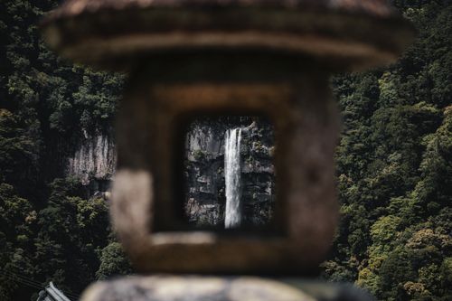 Free A scenic waterfall in Nikkō, Japan, framed by stone architecture, amidst lush green forest. Stock Photo