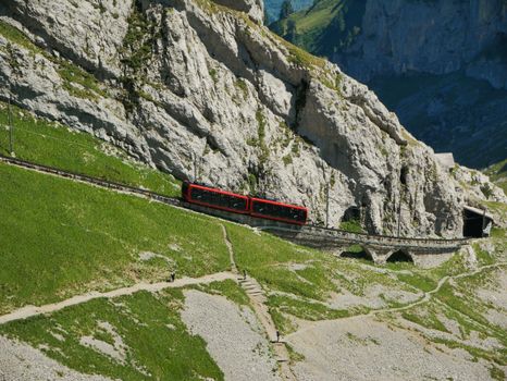 A red cogwheel train travels through the stunning Swiss Alps, showcasing breathtaking mountain views.