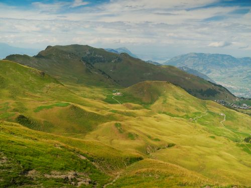 Free A picturesque landscape of green rolling hills in the Swiss Alps under a partly cloudy sky. Stock Photo