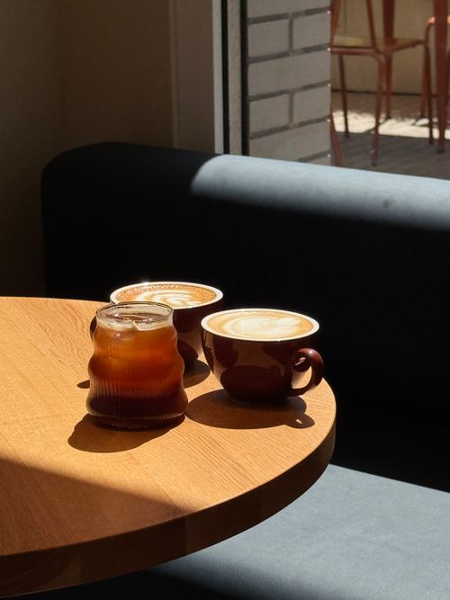 Free Enjoy a serene coffee moment with lattes and iced drink in a sunlit cafe. Stock Photo