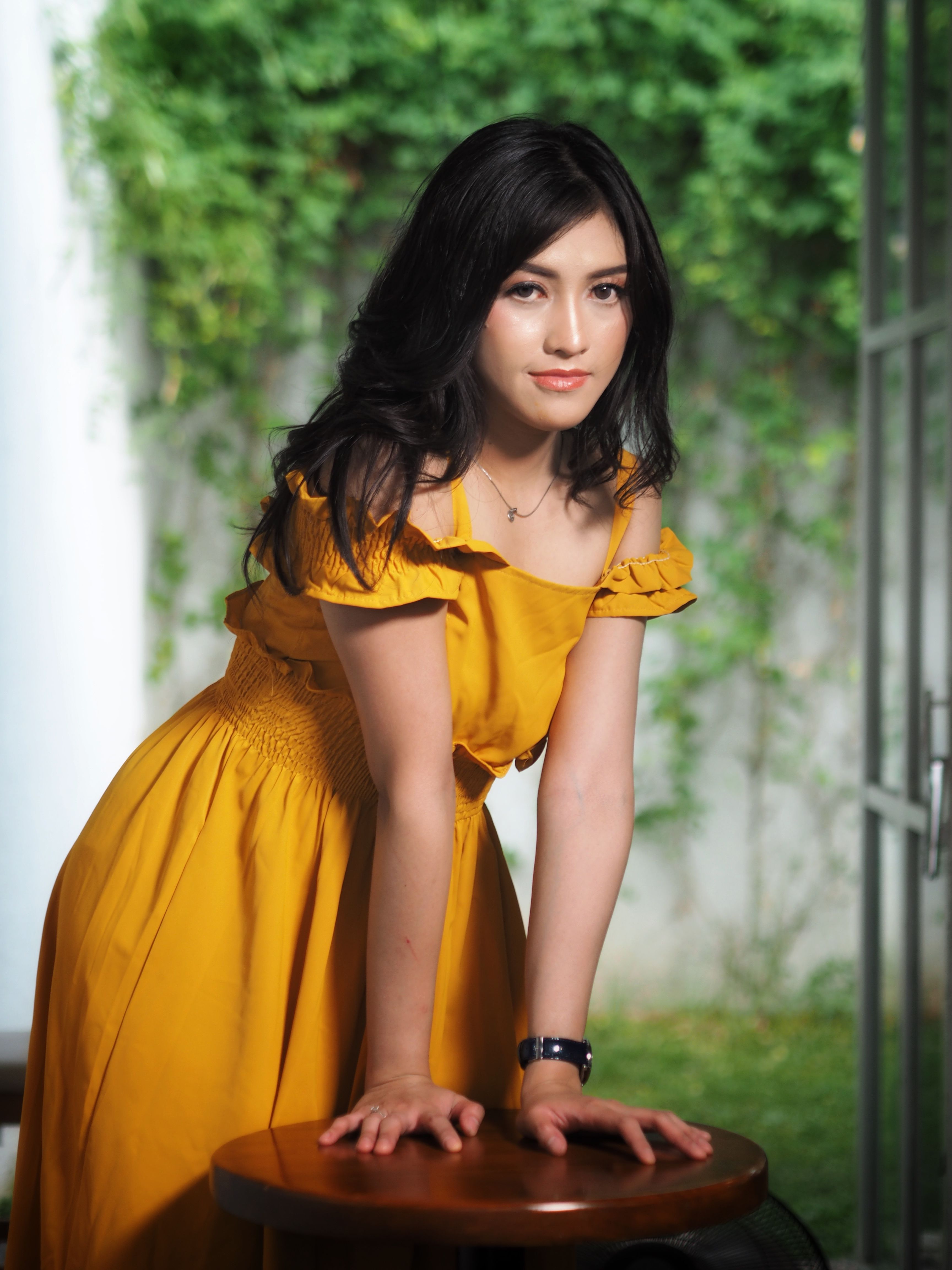 Portrait of a woman in a bright yellow dress indoors with lush greenery.