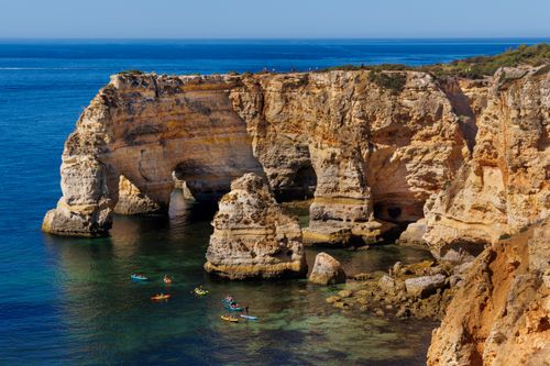 Free Kayakers enjoy the clear waters and scenic rocky cliffs of Algarve, Portugal. Stock Photo