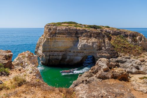 Free Explore the stunning Algarve coastline featuring a natural arch and a boat navigating through clear waters. Stock Photo