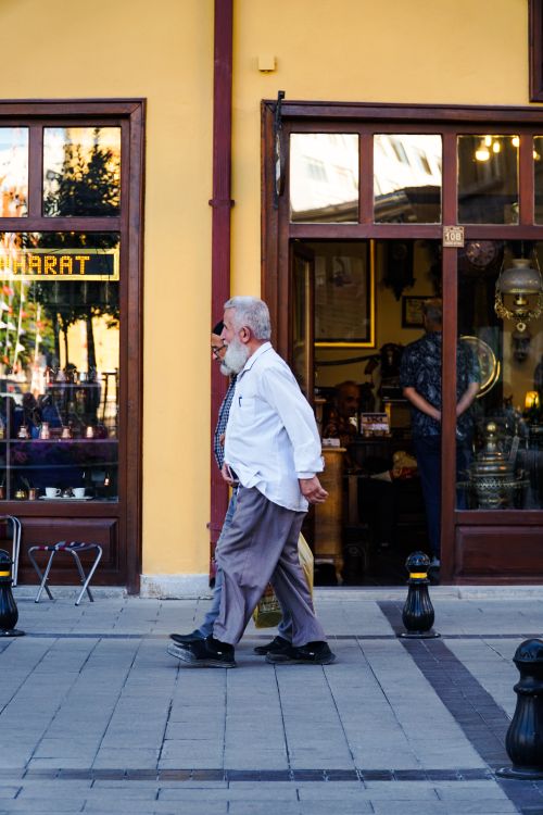 Free A senior man walks by a traditional shop with vibrant displays on a sunny day, capturing everyday life. Stock Photo