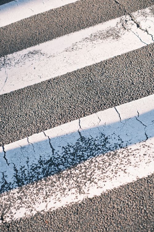 Free Weathered pedestrian crossing on asphalt road with cracked paint and shadows. Stock Photo