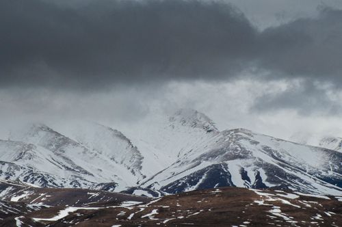 Free Majestic snow-capped mountains under dark, stormy skies, creating a dramatic, high-contrast scene. Stock Photo