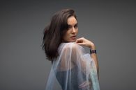 Side view of calm lady covering shoulders with translucent veil and looking at camera while standing in modern studio