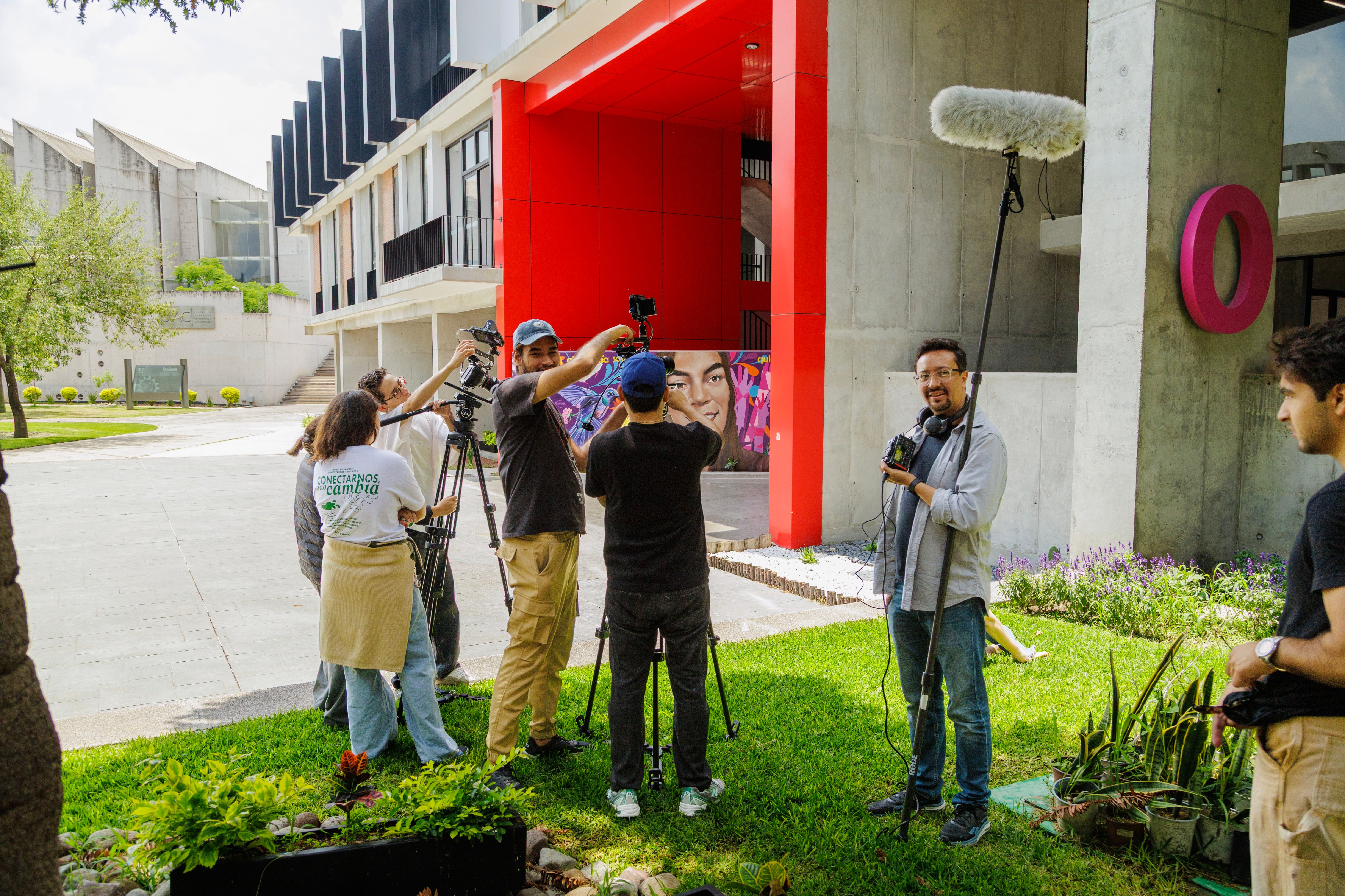 A film crew shooting a documentary outside a modern building with bright red accents.
