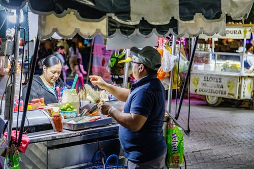 Free A bustling night street food stall with vendors preparing and selling traditional Mexican corn (elotes). Stock Photo