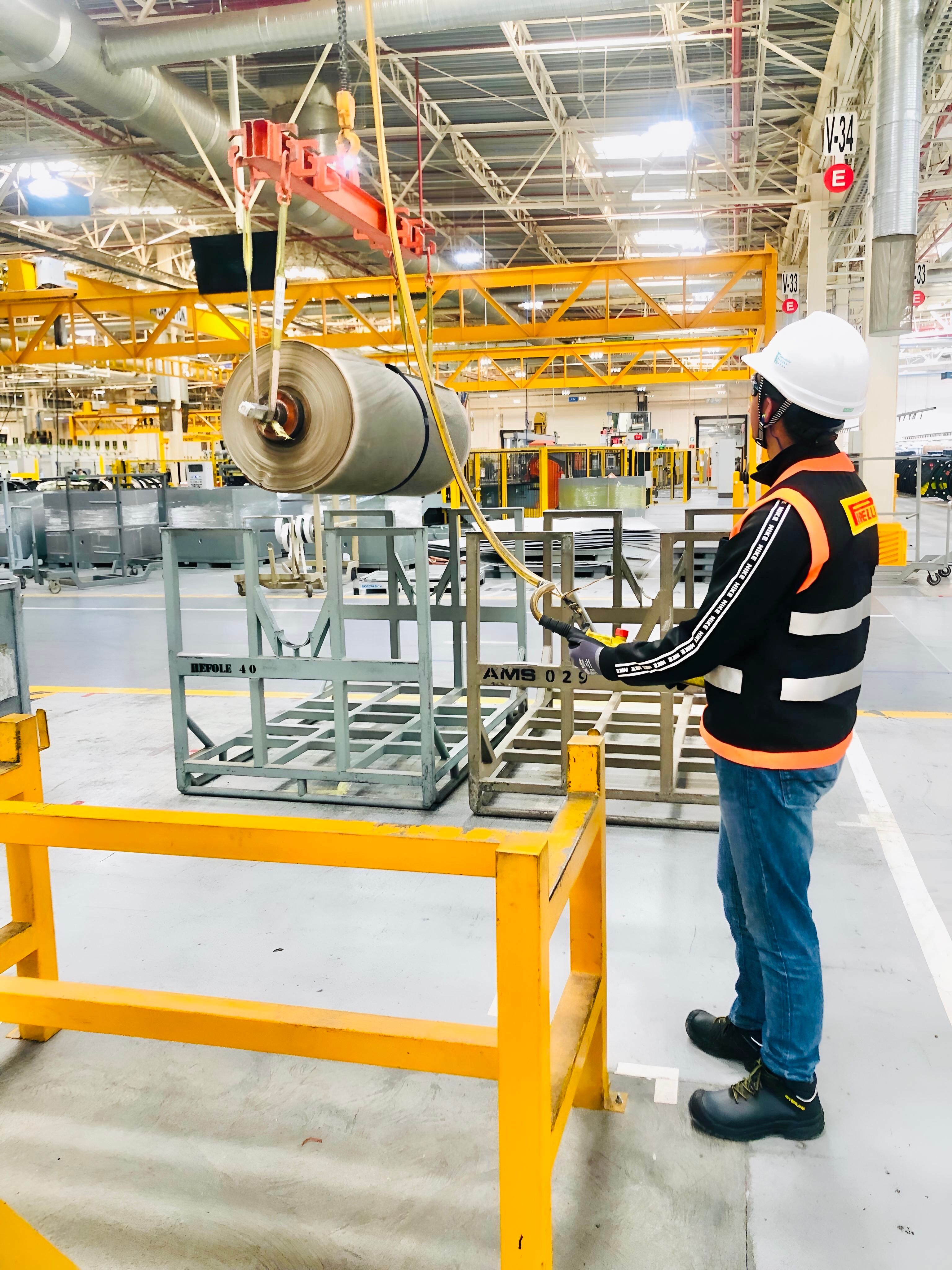 Worker operates a crane in a large industrial factory with safety gear.