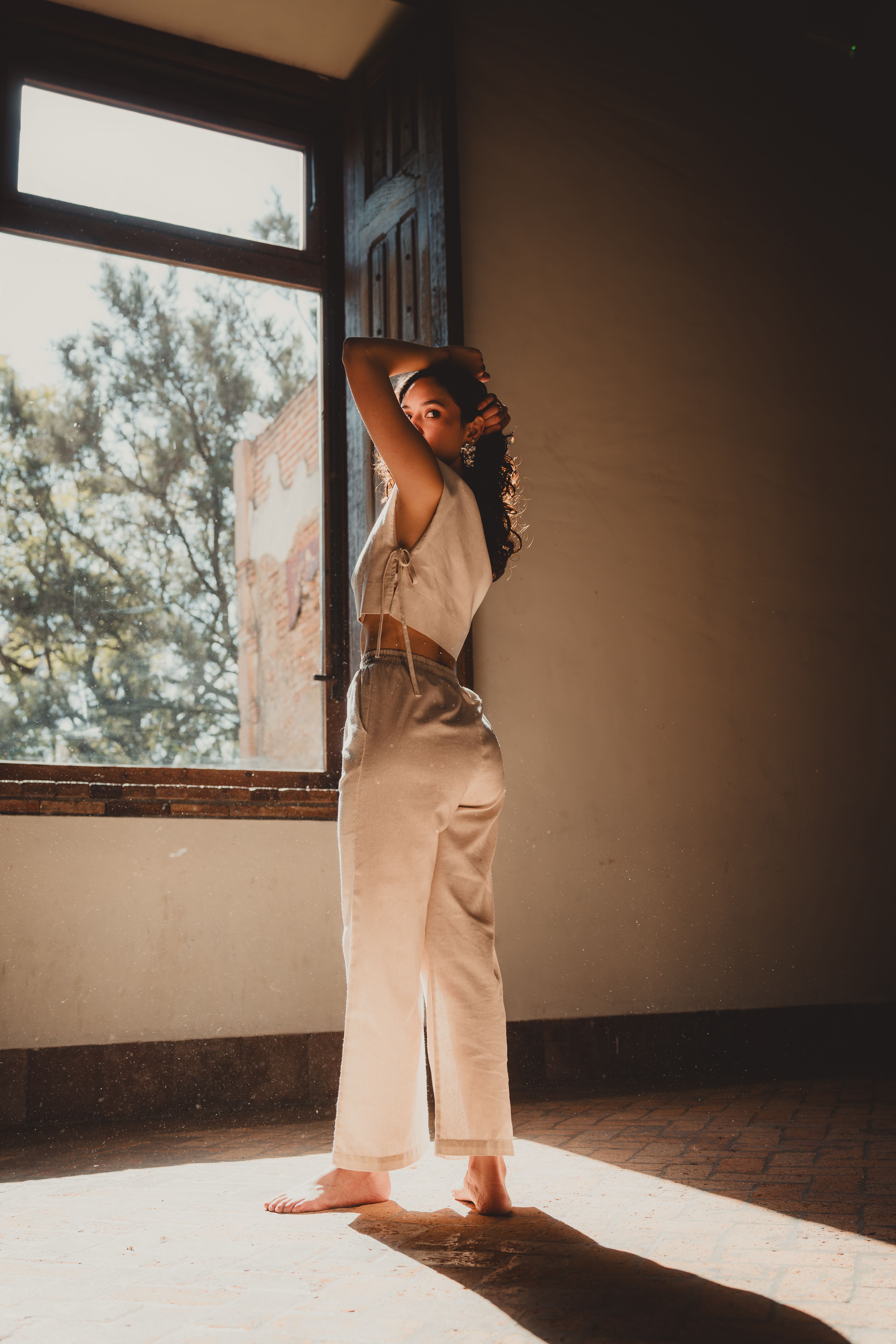 A woman standing in sunlight near an open window, creating a warm and serene atmosphere.