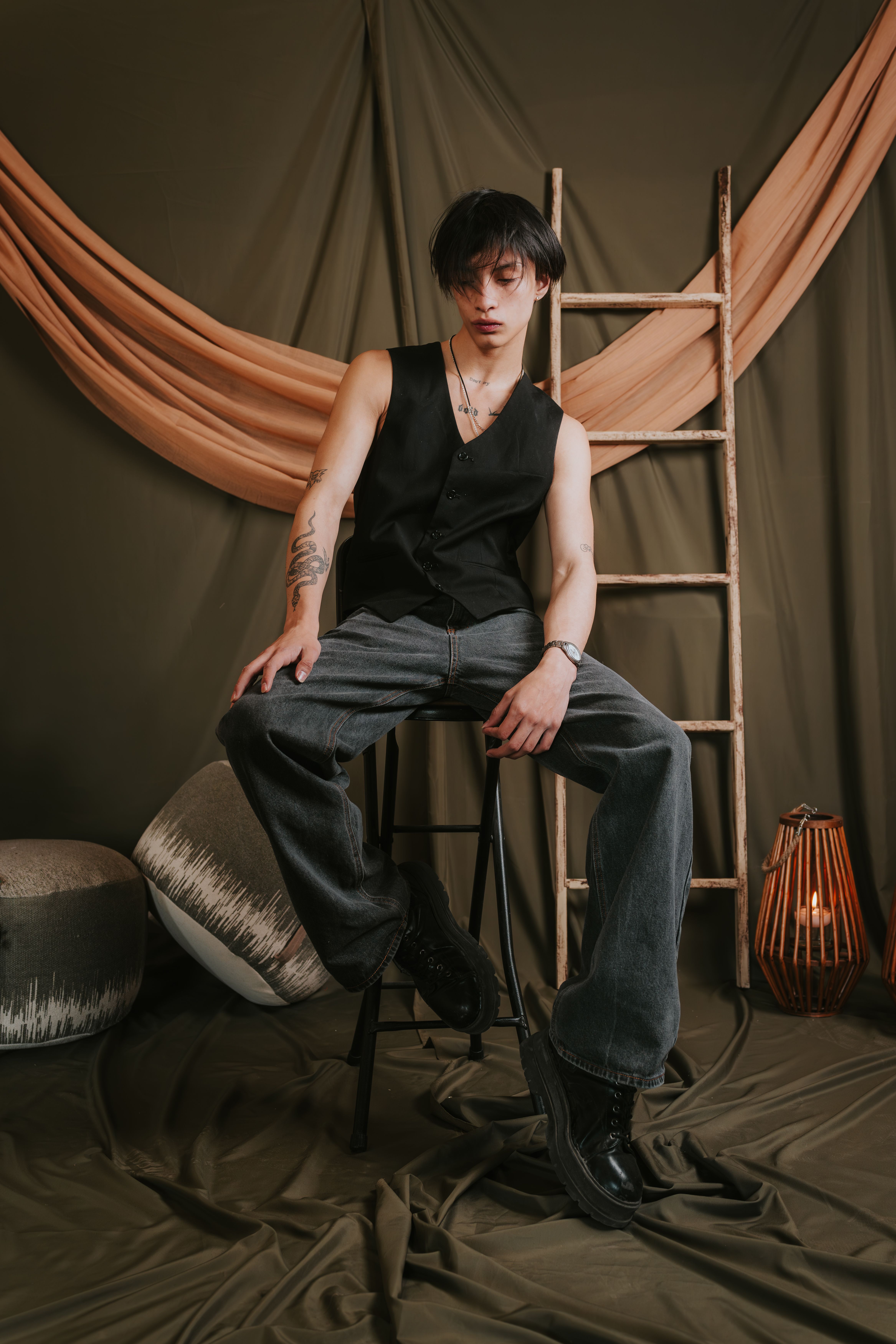 Trendy young man sitting on a stool in a modern, artistic studio setting with warm tones.