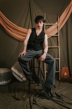 Trendy young man sitting on a stool in a modern, artistic studio setting with warm tones.