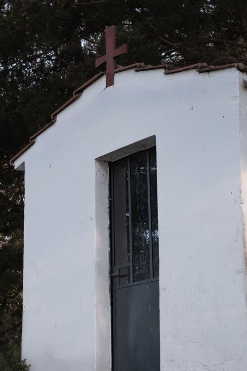 Free Old chapel with a prominent wooden cross on its roof, surrounded by trees. Stock Photo