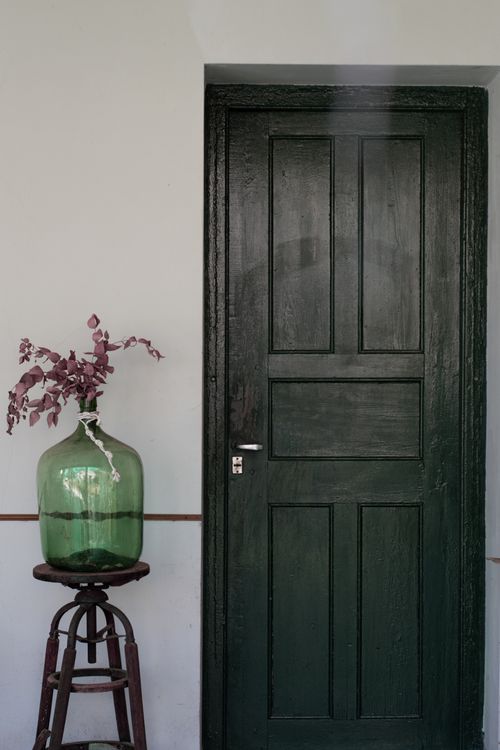 Free Dark wooden door beside a green glass vase on stool, offering a rustic and minimalist aesthetic. Stock Photo