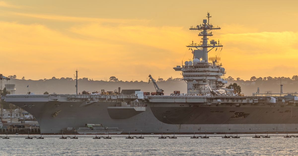 Large aircraft carrier docked at a harbor during a vibrant sunset, creating a dramatic nautical scene.