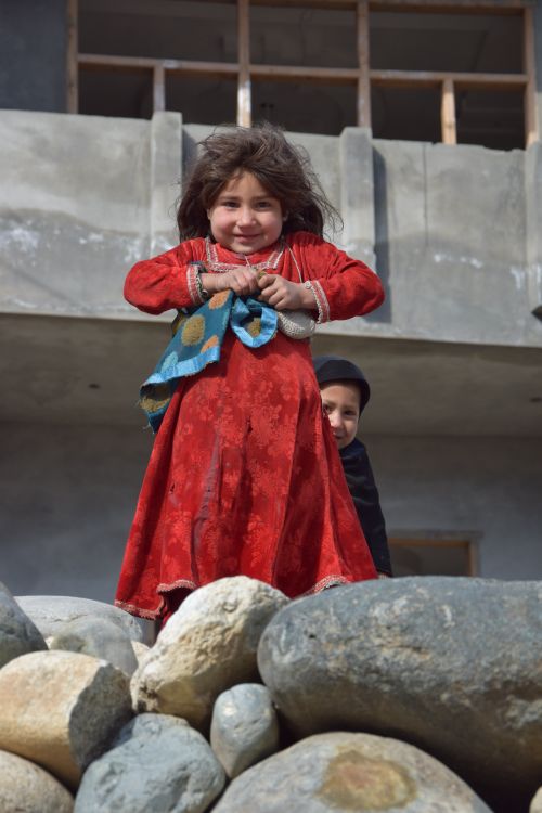 Free A cheerful child in a red dress stands on rocks, brightening the scene. Stock Photo