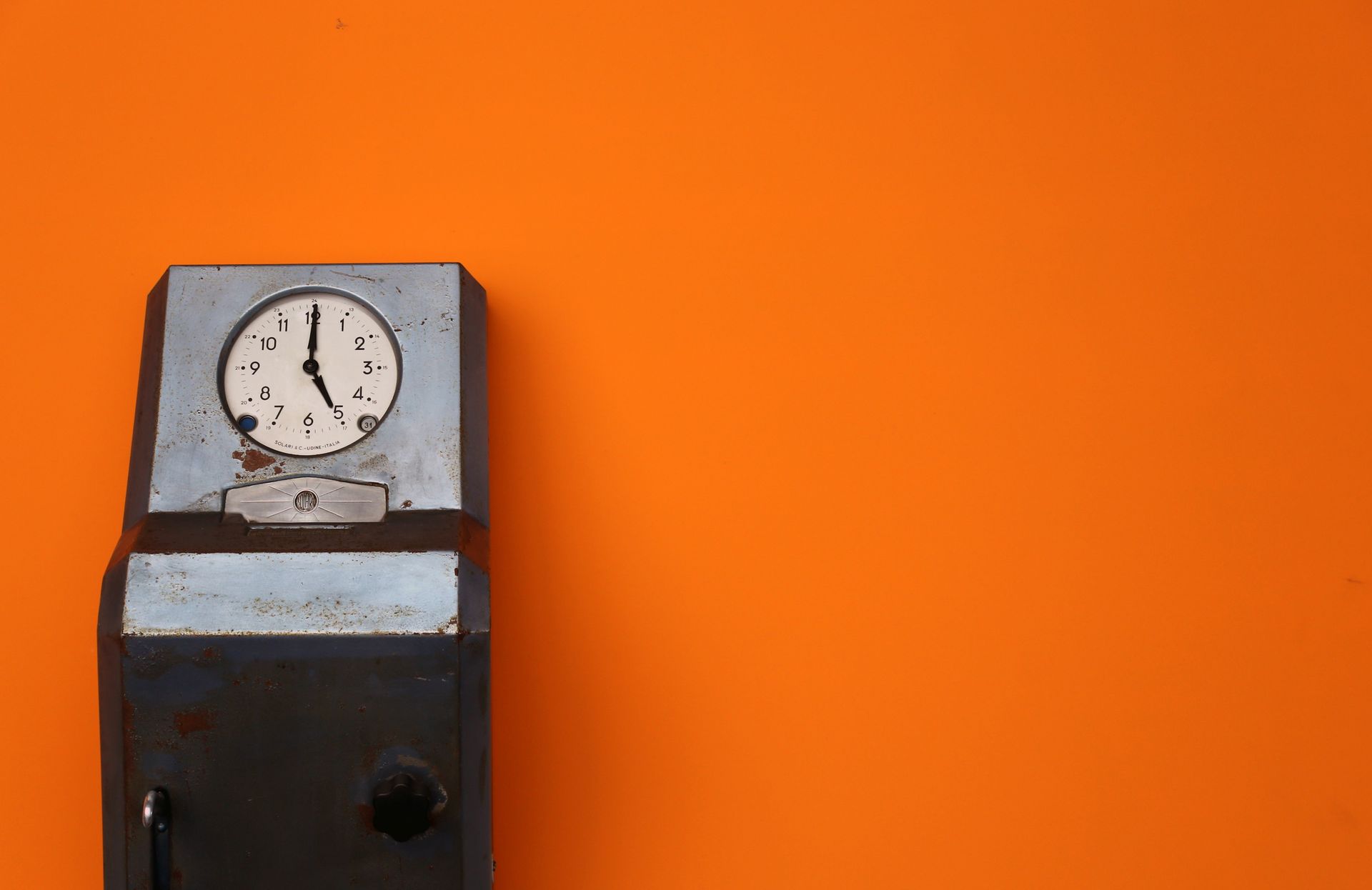 Close-up of a vintage analog clock against a vibrant orange background. Ideal for time-related themes.