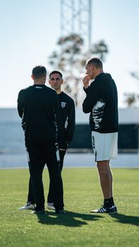 Three soccer coaches discussing strategies on a sunny outdoor field.