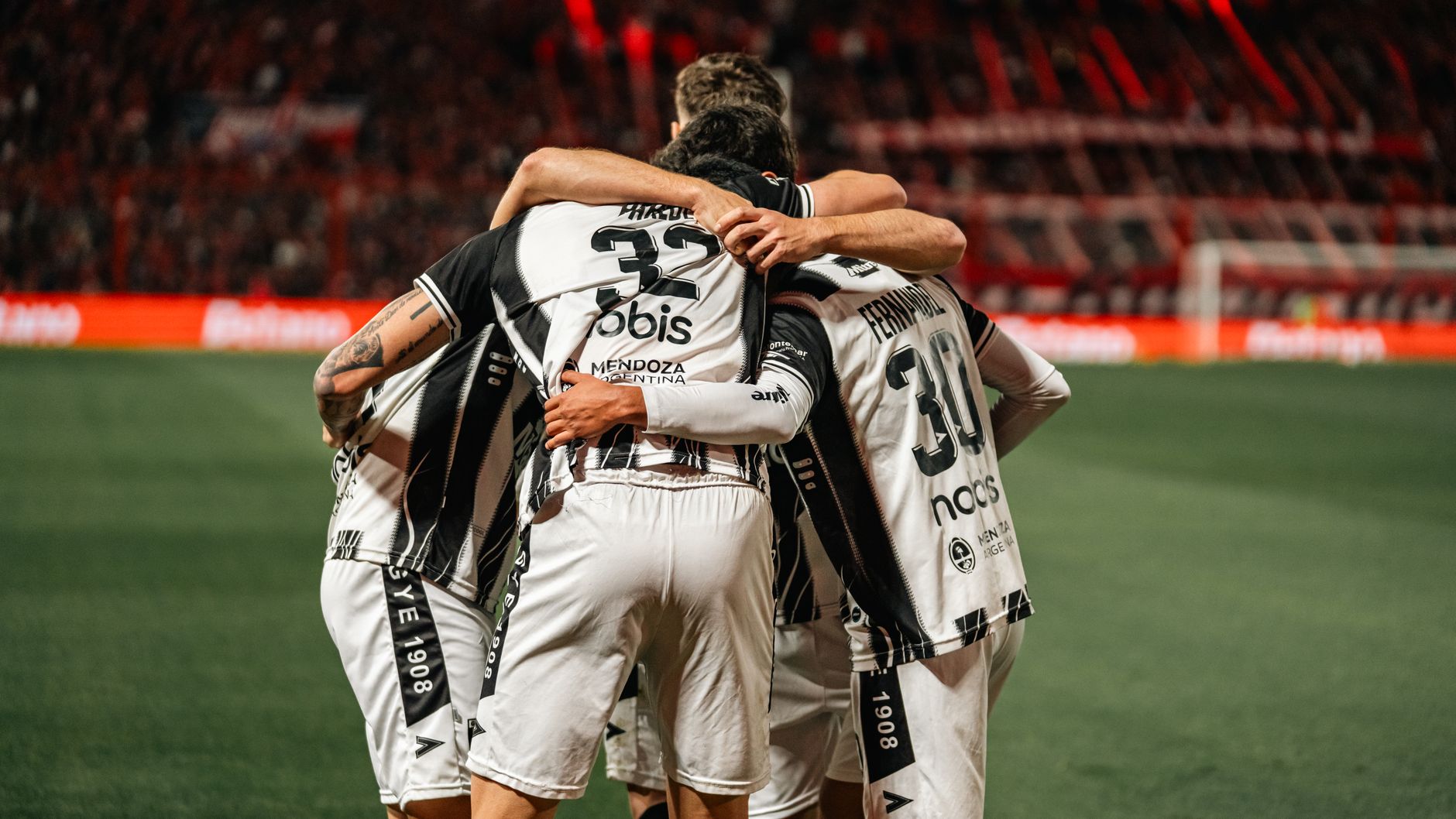 Soccer players in black and white jerseys celebrating a victory with a group hug on the field.