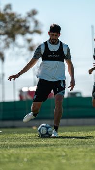 A male soccer player dribbles a ball on a sunny outdoor field during practice.
