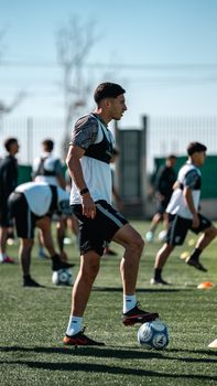Group of young men practicing soccer drills on an outdoor field on a sunny day.