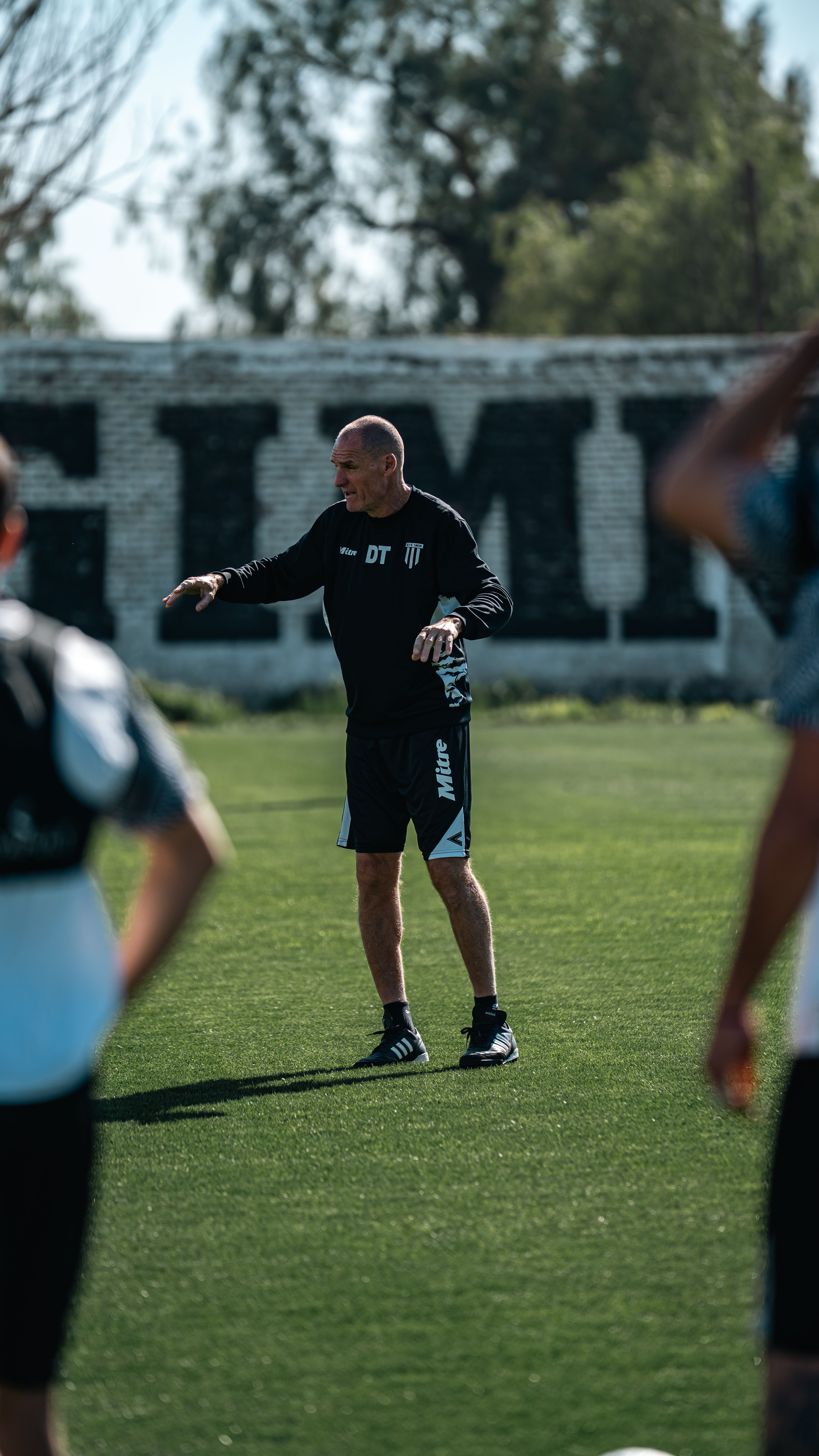 Football coach instructing players during practice on a sunny field.