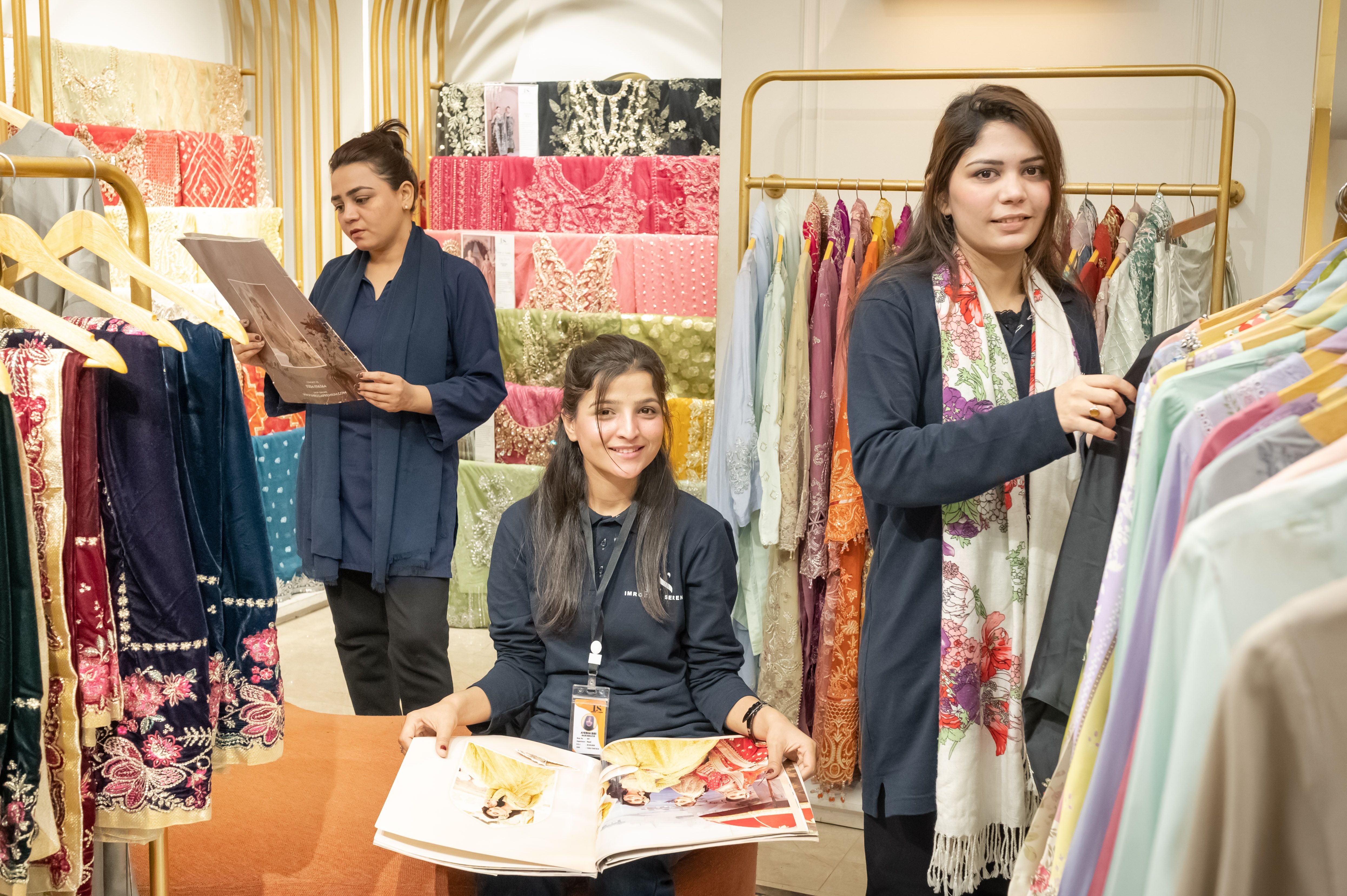 Three women looking at colorful fabrics in a clothing store, showcasing vibrant textile designs.
