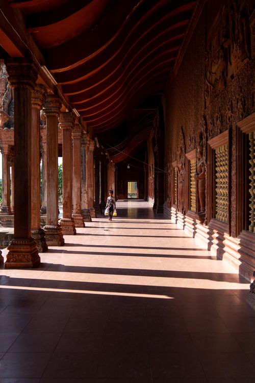 Free A lone person walks through a sunlit temple corridor with ornate pillars and walls, highlighting architectural beauty. Stock Photo