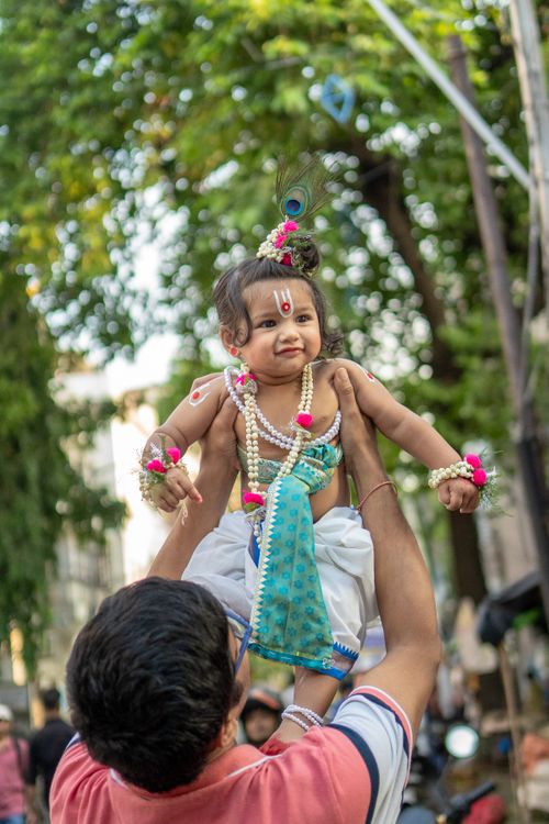 Free A baby dressed as Lord Krishna is lifted in a festive outdoor setting, capturing a joyful religious celebration. Stock Photo