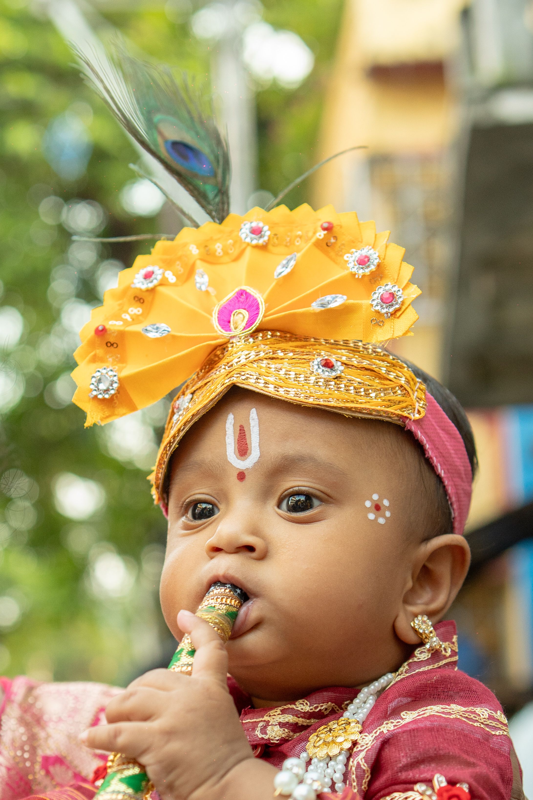Adorable baby in a Krishna costume holding a flute, outdoors.