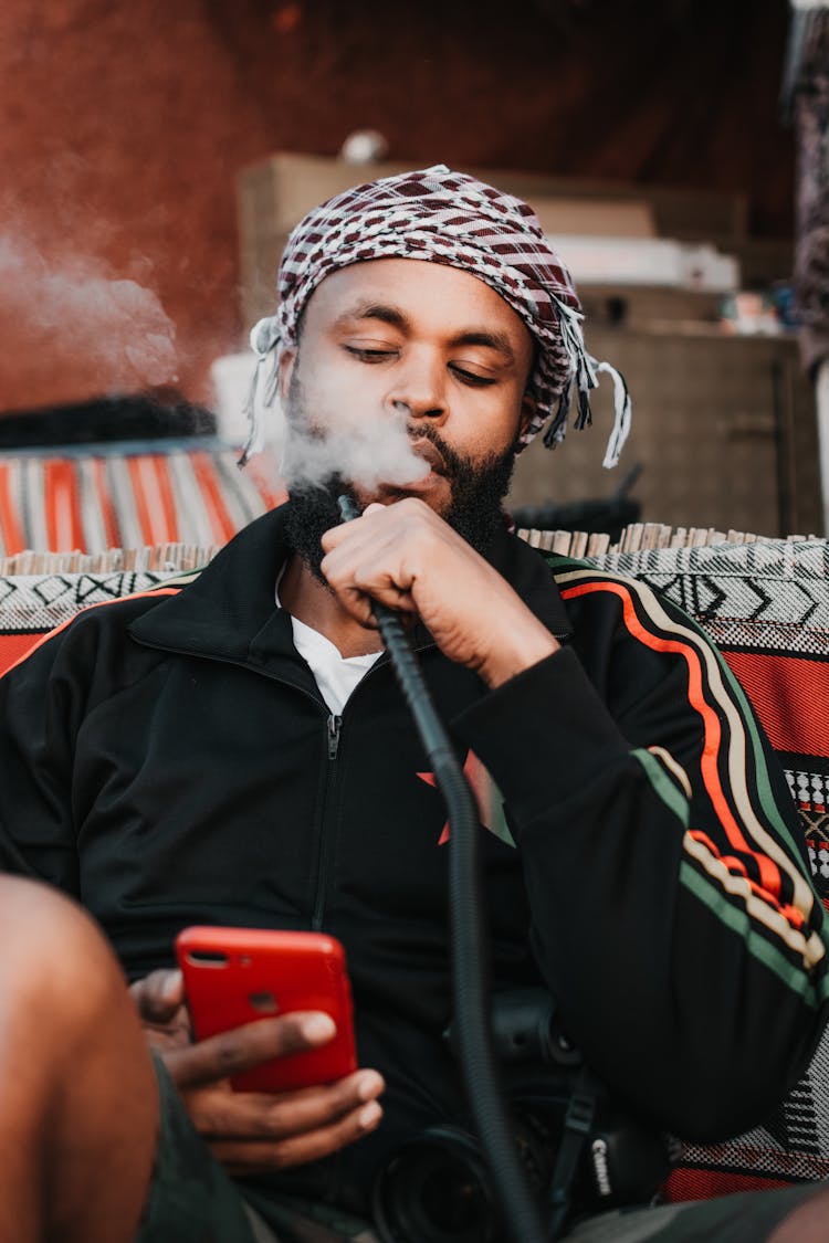 Man Using Shisha While Looking At Phone