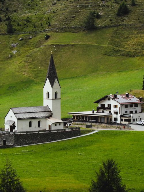 Free A picturesque view of a traditional church in Trentino-Alto Adige surrounded by lush green hills. Stock Photo