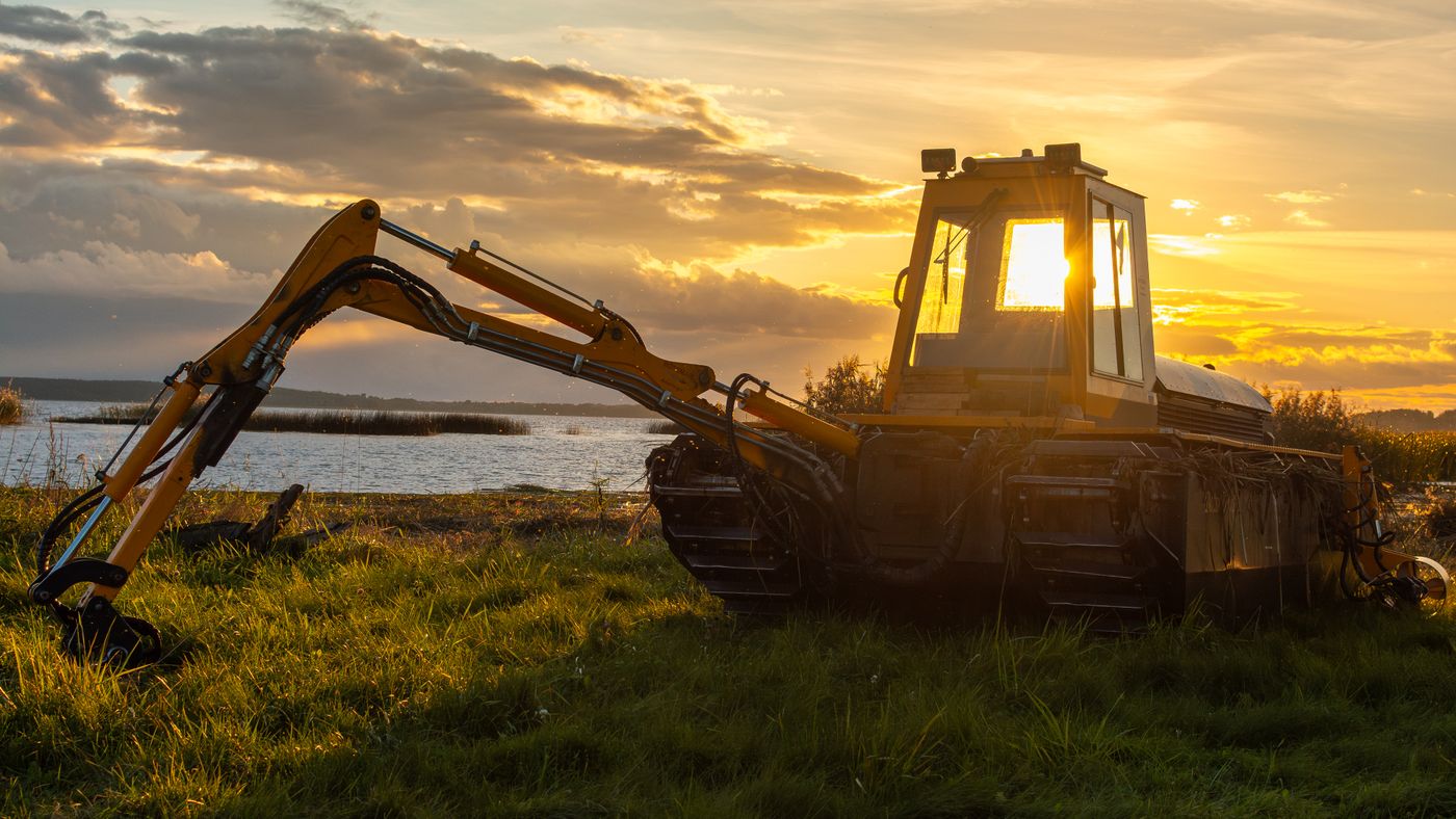 Excavator silhouetted at sunset beside a lake