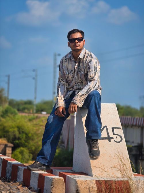 Free Young man in sunglasses poses casually on a concrete marker against a clear blue sky. Stock Photo