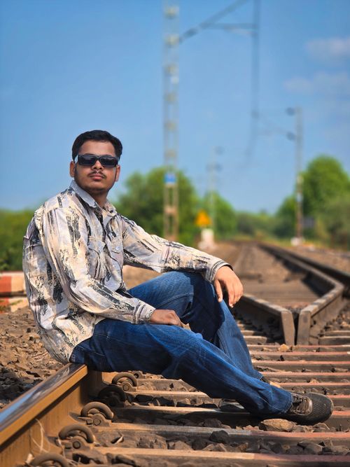 Free Young man wearing sunglasses sitting on railroad tracks in a casual pose, outdoors. Stock Photo