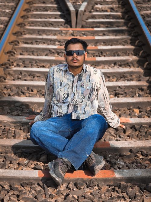 Free Man sitting casually on railway tracks with sunglasses and casual attire. Stock Photo