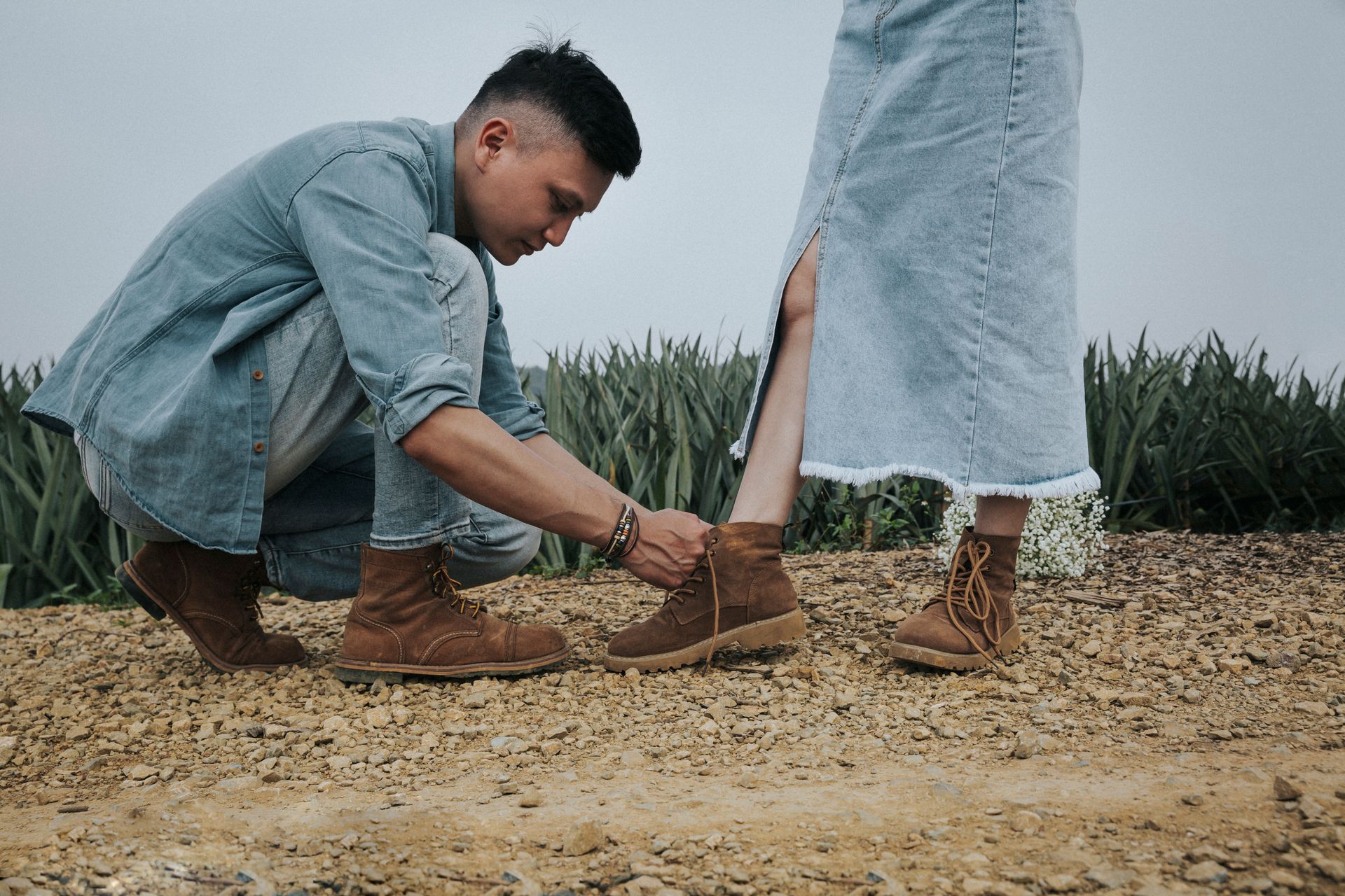 A man helps a woman tie her boots on a rural path in Ninh Bình, Vietnam.